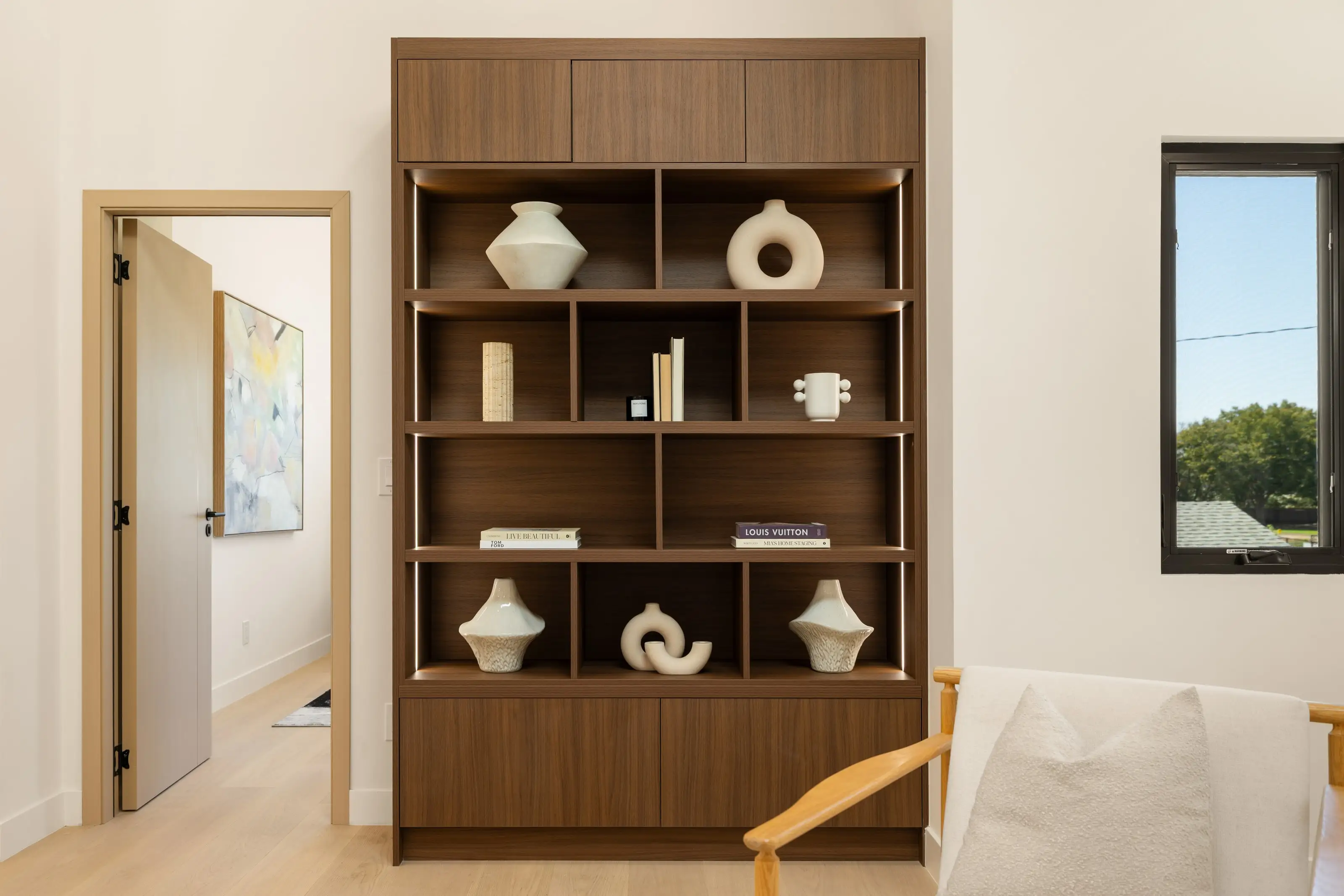 Walnut built-in display shelving with integrated LED lighting, flat panel doors above and below, styled with ceramics and books