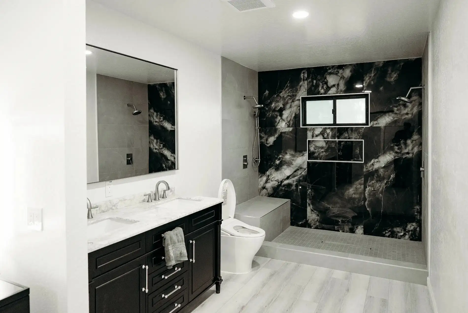 Remodeled bathroom with black marble shower walls, dark vanity, white countertop, and walk-in shower with bench seat