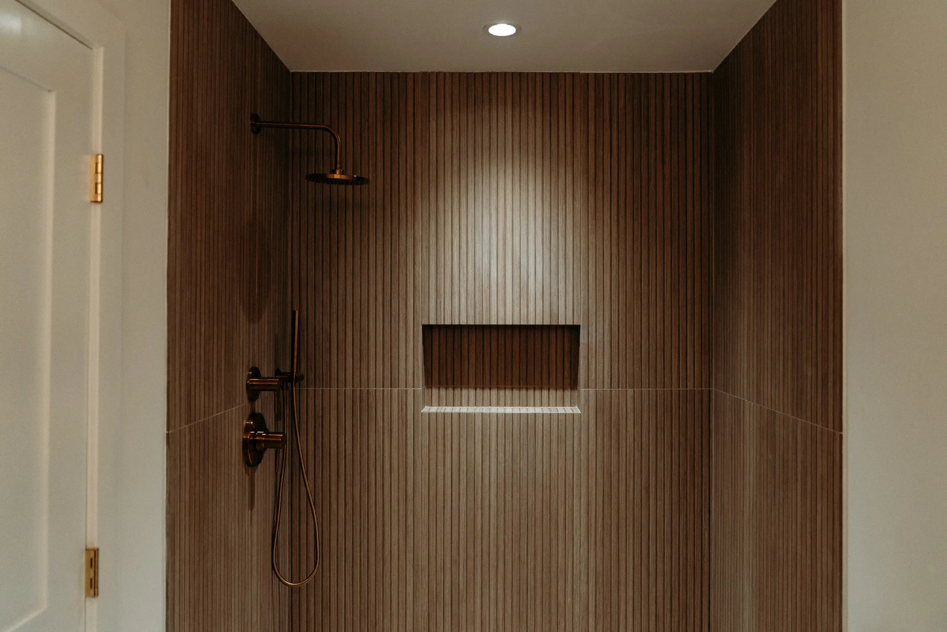 Modern shower remodel with ribbed wood-look tile walls, bronze rain shower head, hand shower, and recessed niche shelf