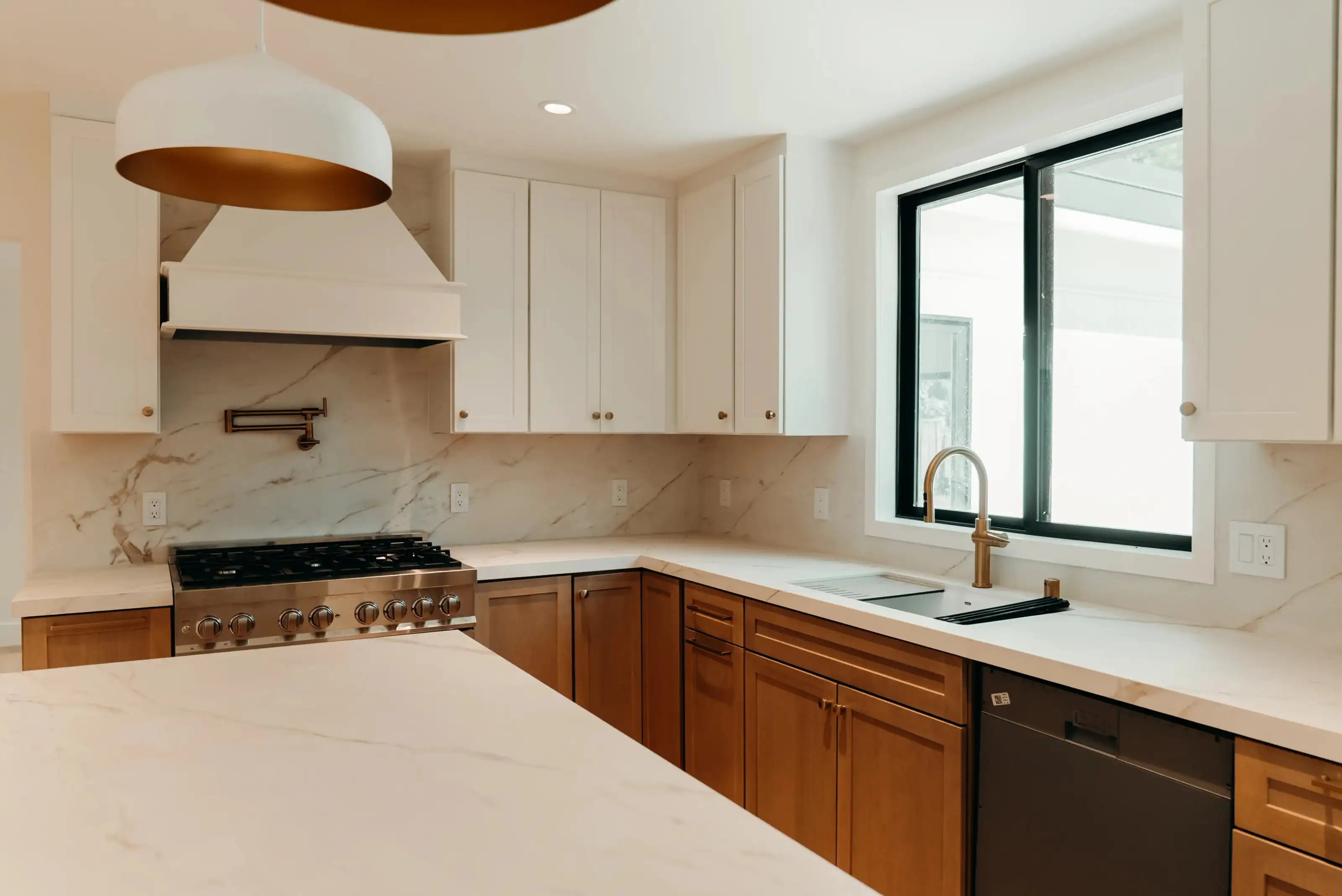 Kitchen remodeling project with white upper cabinets, warm wood lower cabinets, marble backsplash, stainless gas range, and