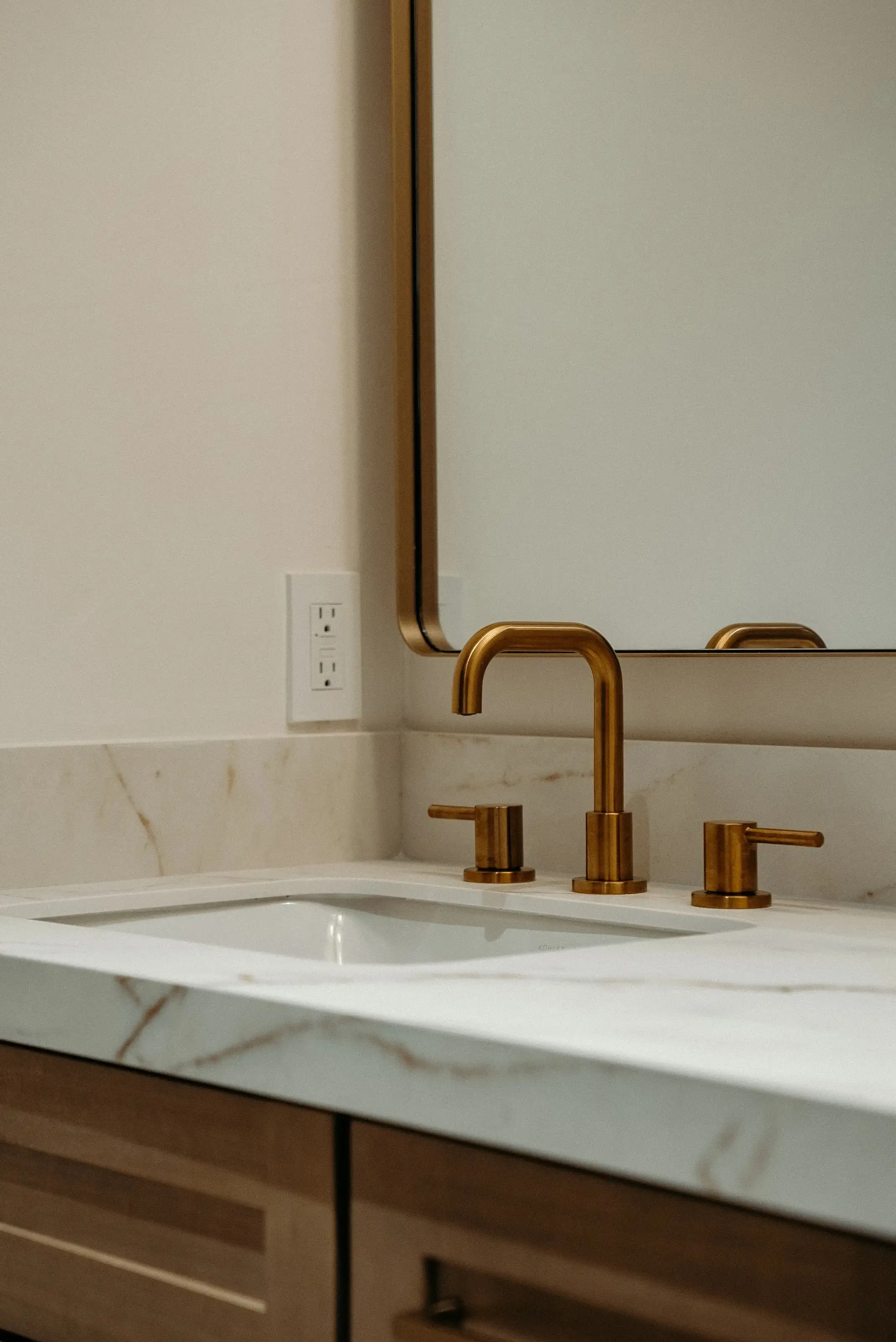 Brushed brass widespread faucet with two handles on a white marble bathroom vanity countertop during bathroom remodeling