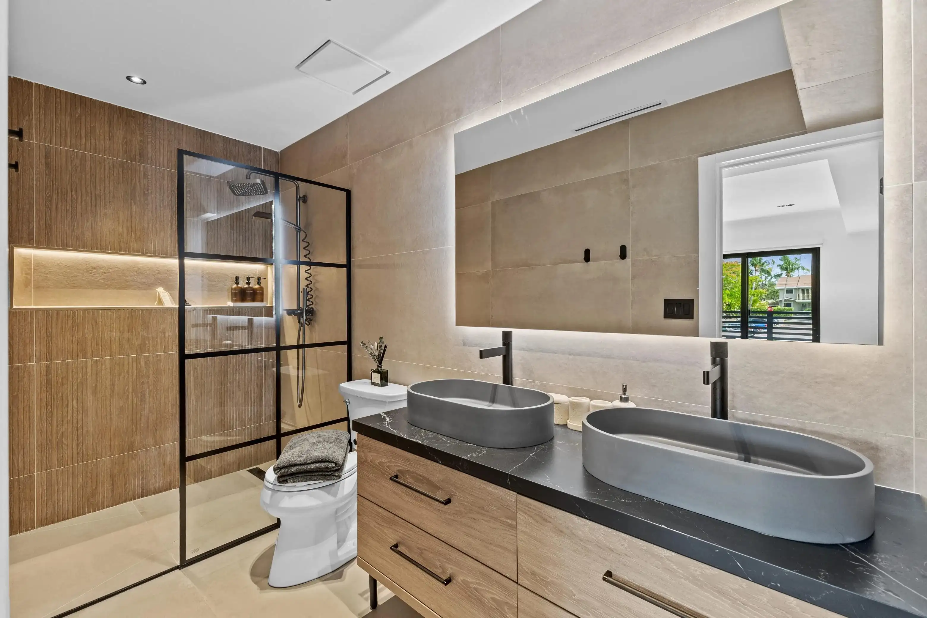 Modern bathroom remodel with double gray vessel sinks on black marble vanity, wood cabinets, and glass shower enclosure