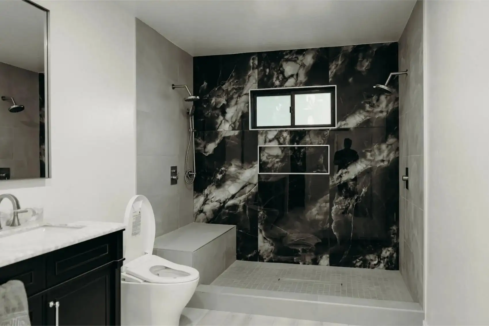 Bathroom remodel with black marble shower walls, dual rain shower heads, built-in niche, and white toilet in San Jose / Bay