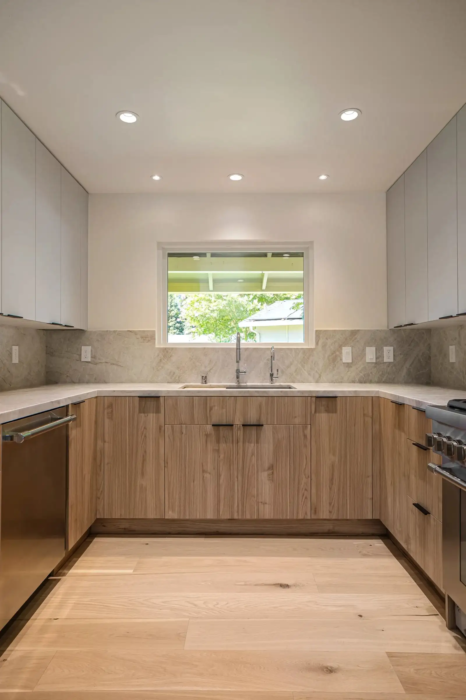 Modern kitchen remodel with wood lower cabinets, white upper cabinets, marble backsplash, and stainless steel sink under a