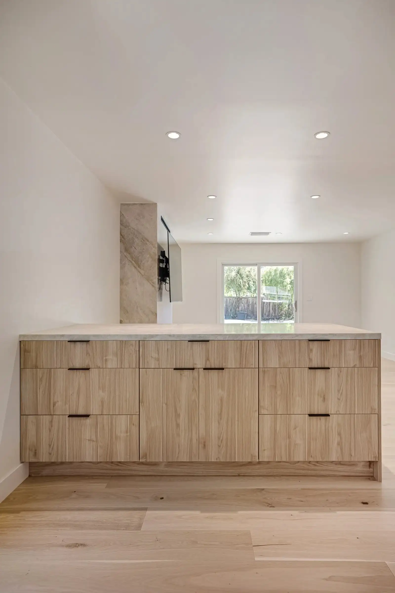 Kitchen island with light wood grain drawers, gray stone countertop, and marble tile pillar during kitchen remodeling