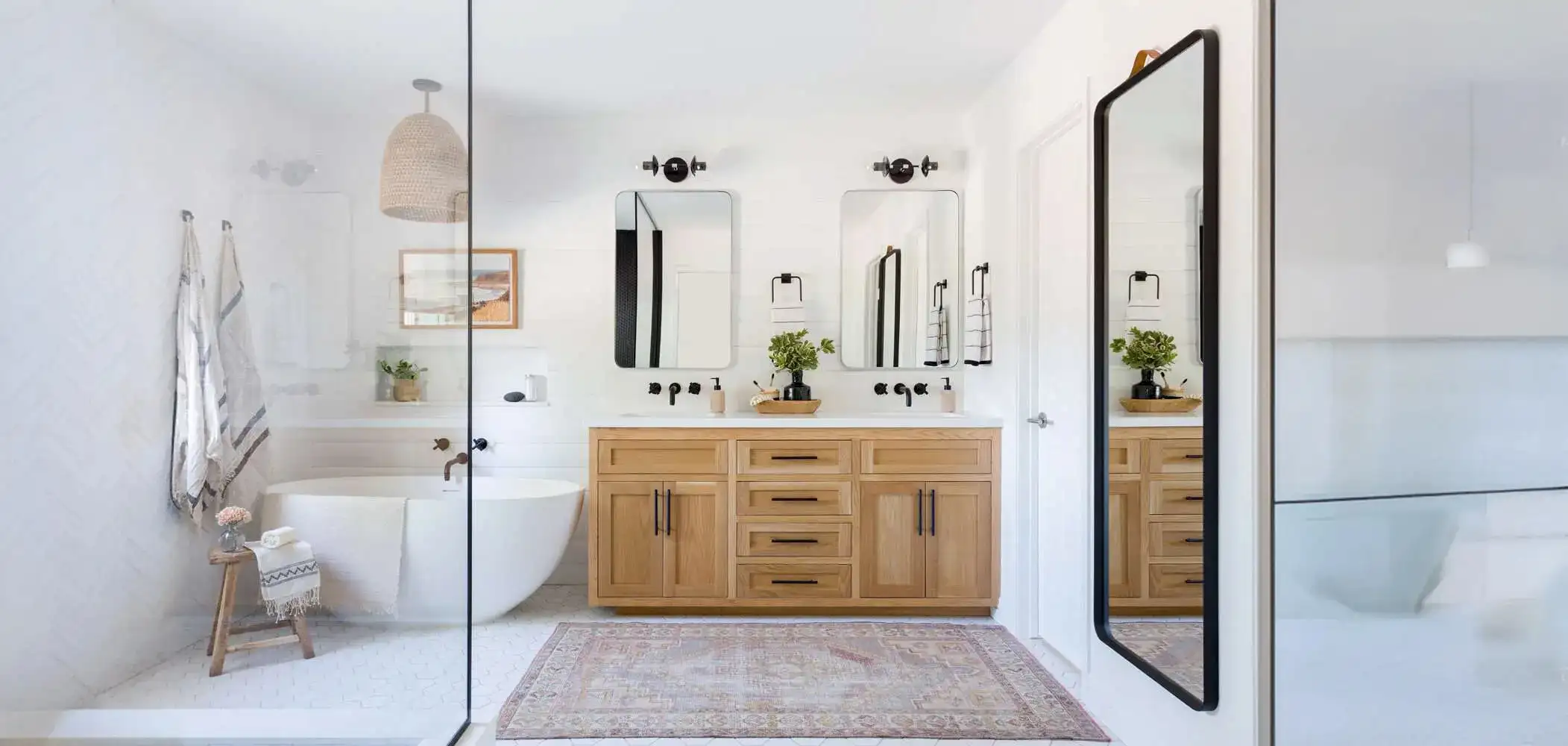 Double sink wood vanity with black hardware, two mirrors, and freestanding tub in a bathroom remodel