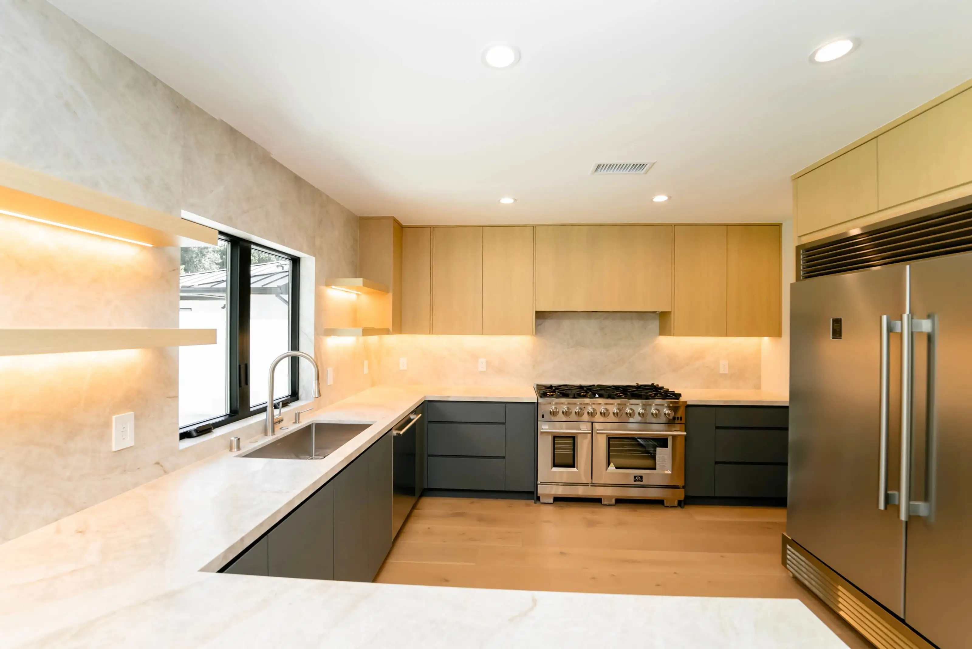 Modern kitchen remodeling in San Jose featuring light wood cabinets, marble countertops, and stainless steel appliances with warm ambient lighting