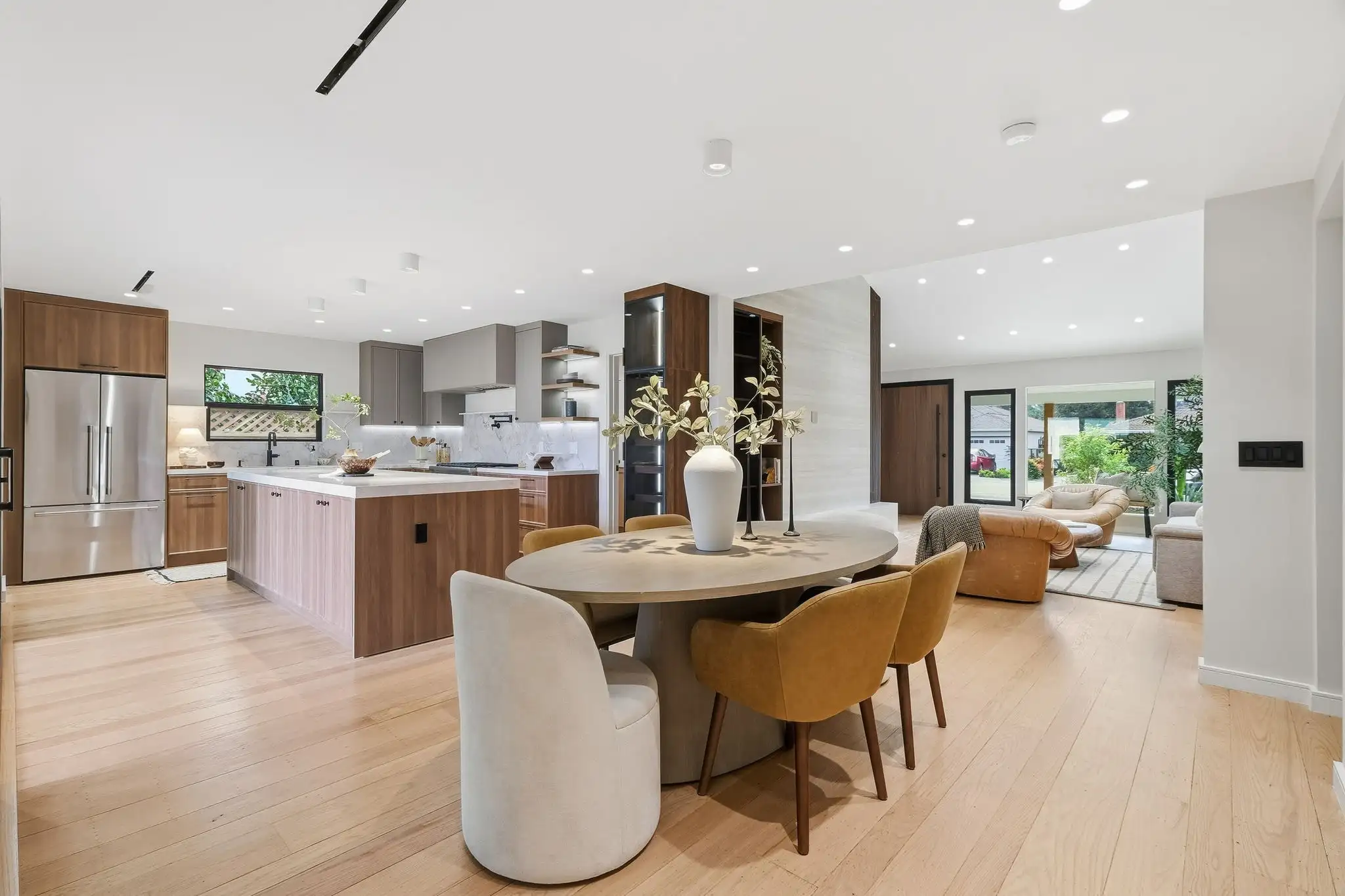 Open-concept dining area and kitchen remodel with round table, mixed seating, wood cabinetry, and light hardwood floors