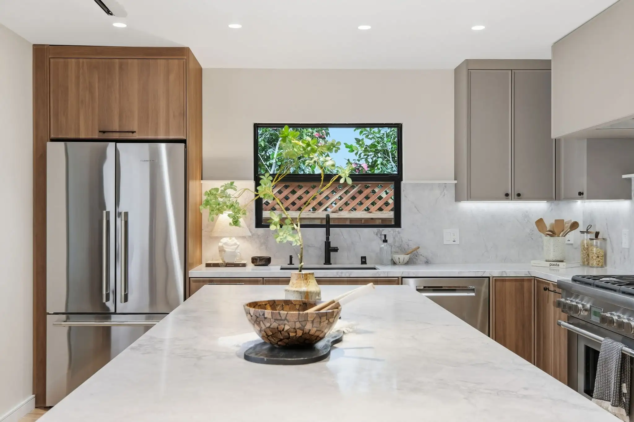 Modern kitchen remodel with marble island, walnut cabinets, stainless refrigerator, black faucet, and window above sink