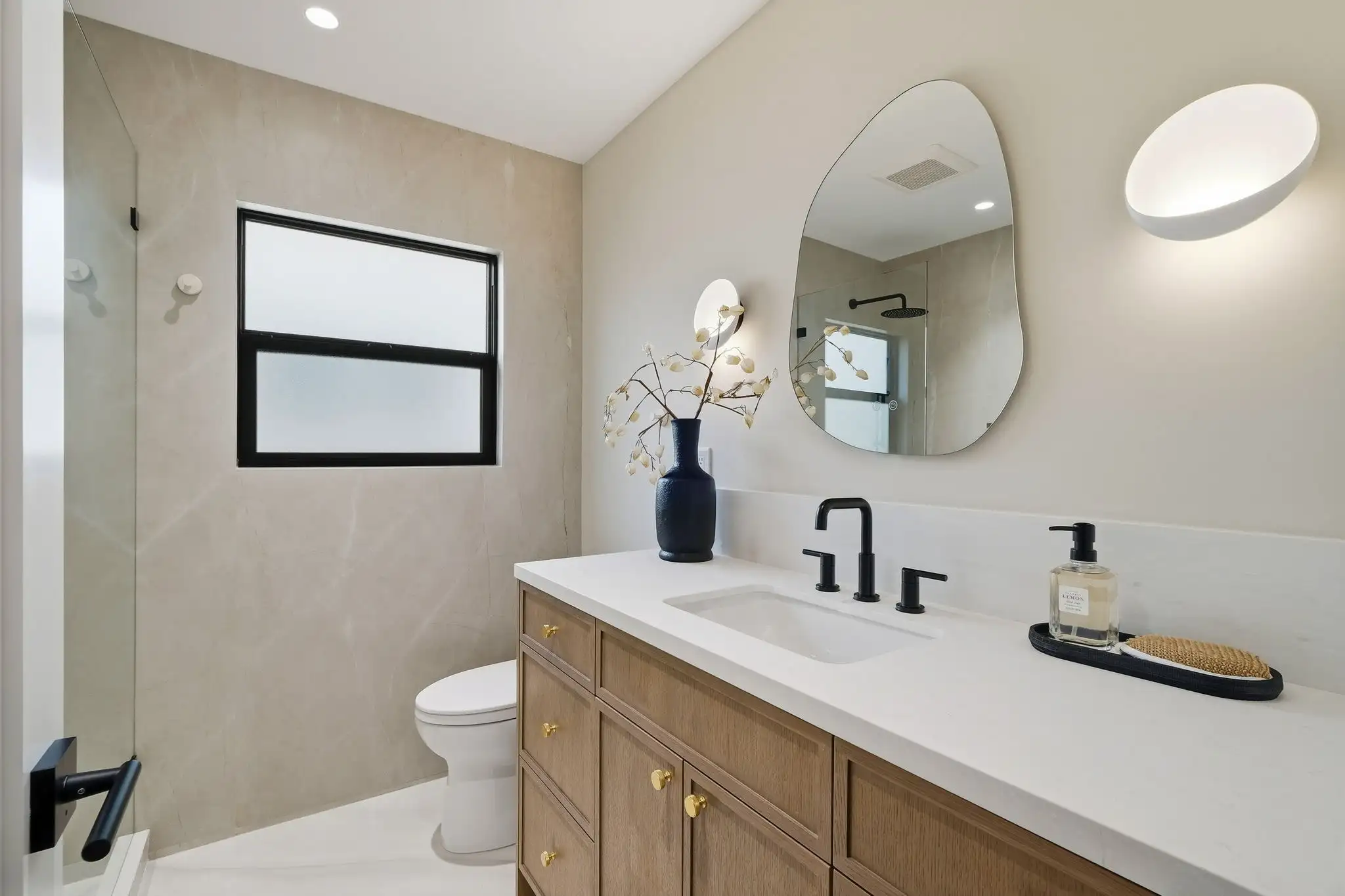 Bathroom remodel with wood vanity, white quartz countertop, matte black faucet, gold hardware, organic mirror, and walk-in