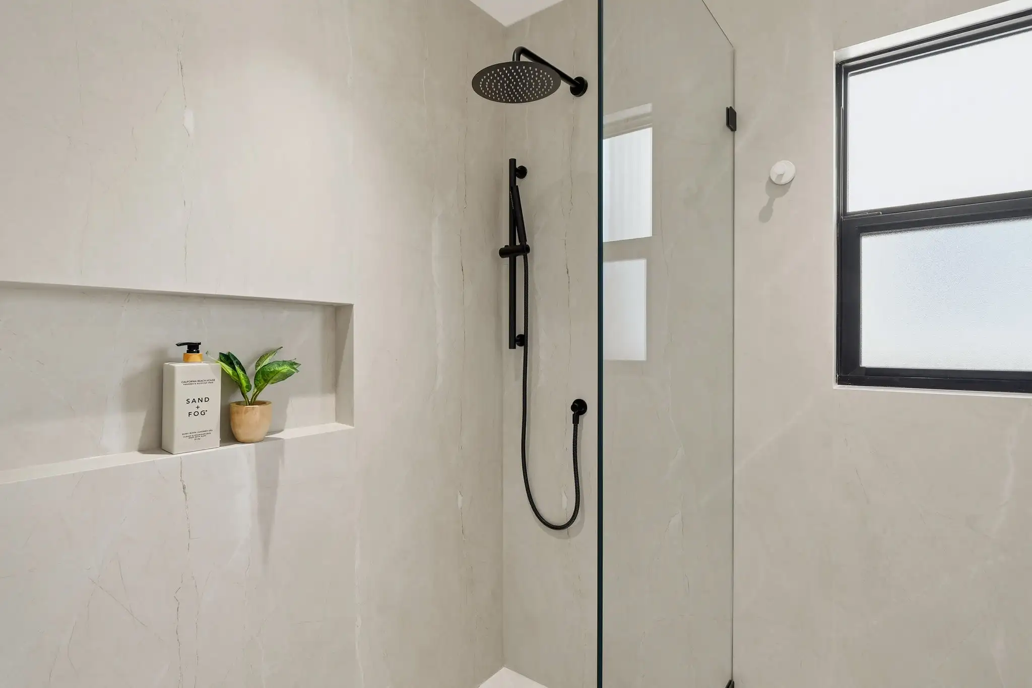 Walk-in shower remodel with matte black rain showerhead, handheld wand, frameless glass panel, and built-in tile niche with