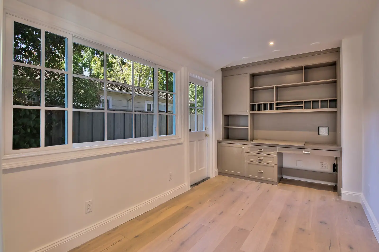 Built-in desk with shaker drawers and open shelving beside a wide window seat