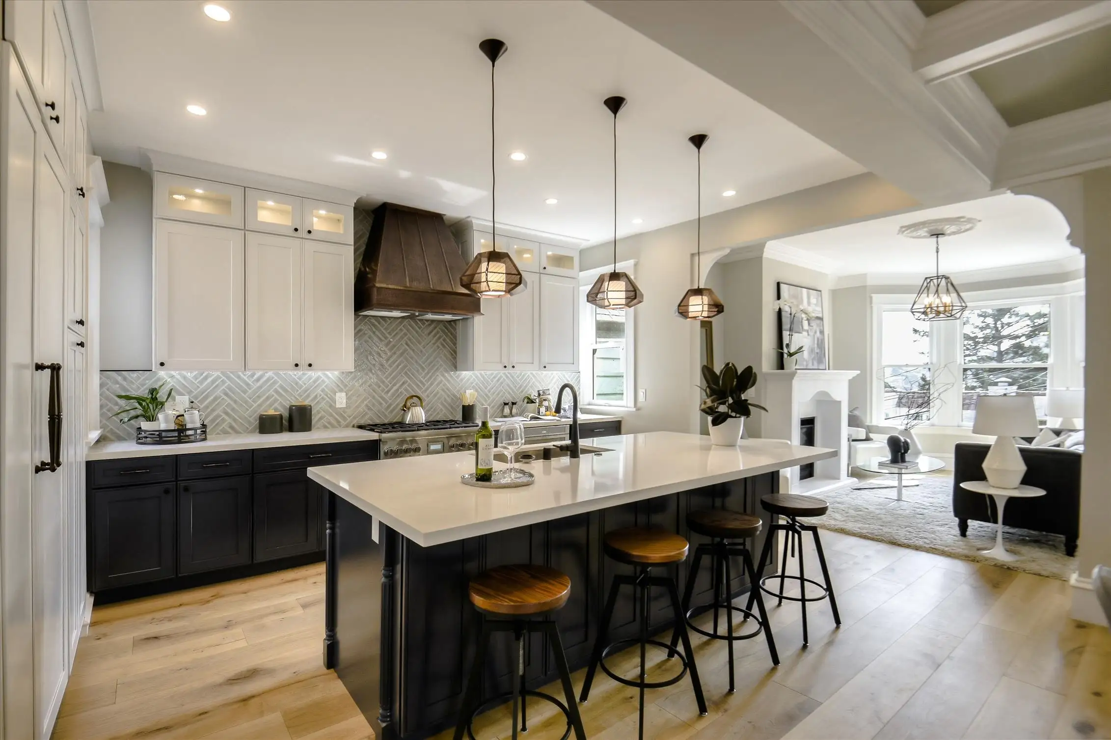White shaker kitchen with a dark island, wood hood, brass pendants and herringbone backsplash
