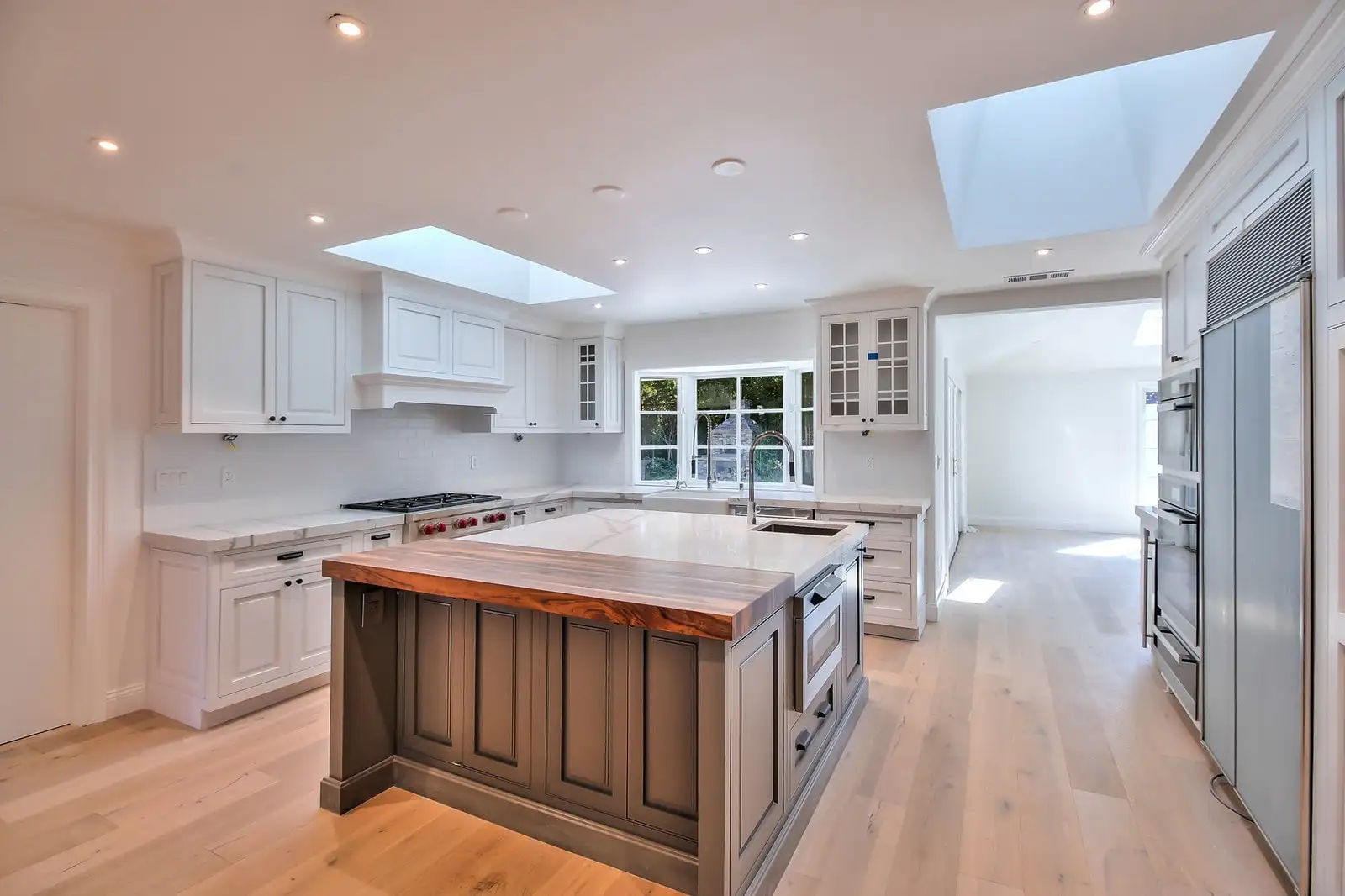 White shaker kitchen with a walnut island, butcher block top and a skylight over the run