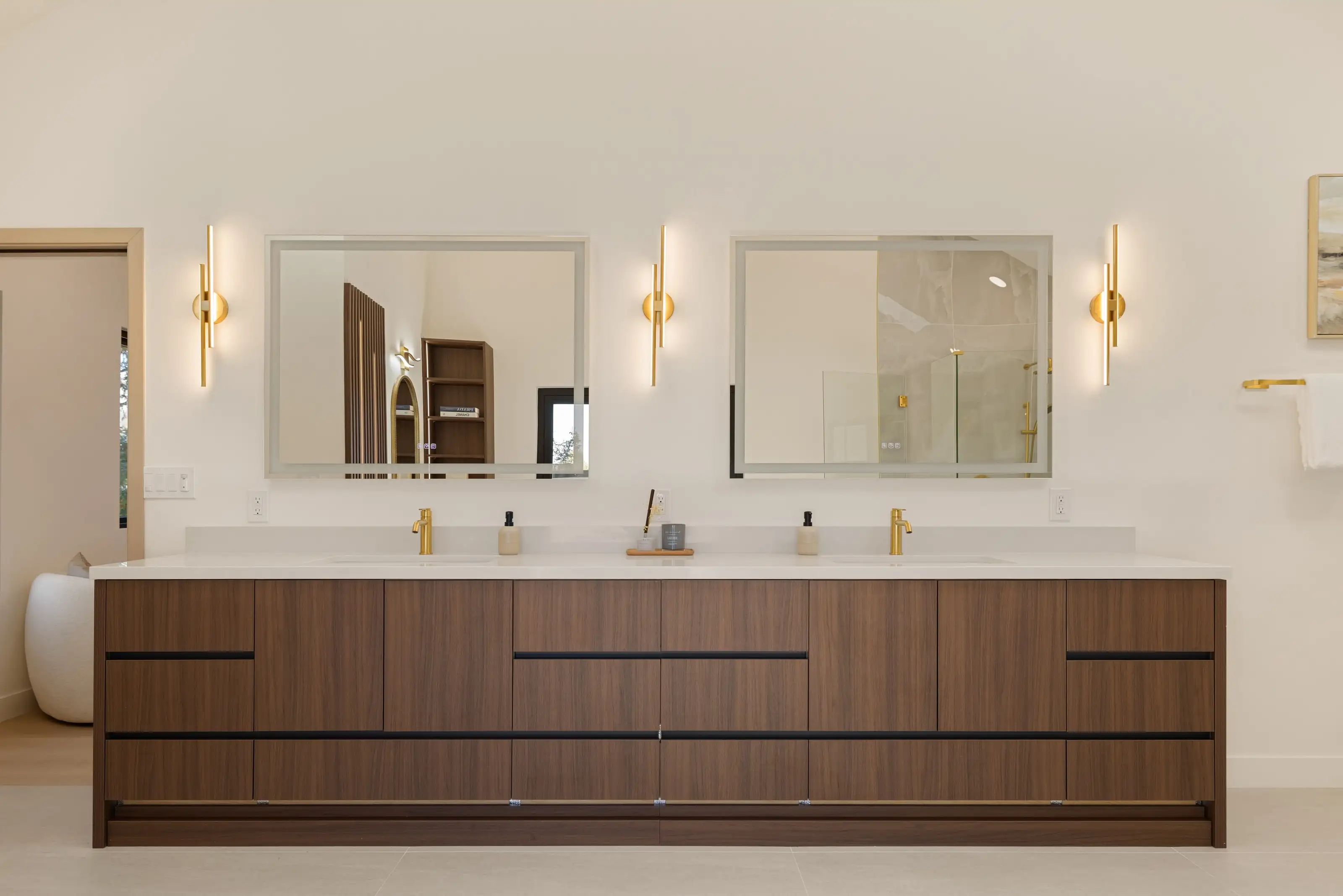 Walnut double vanity with a white quartz top, brass faucets, paired mirrors and three linear brass sconces